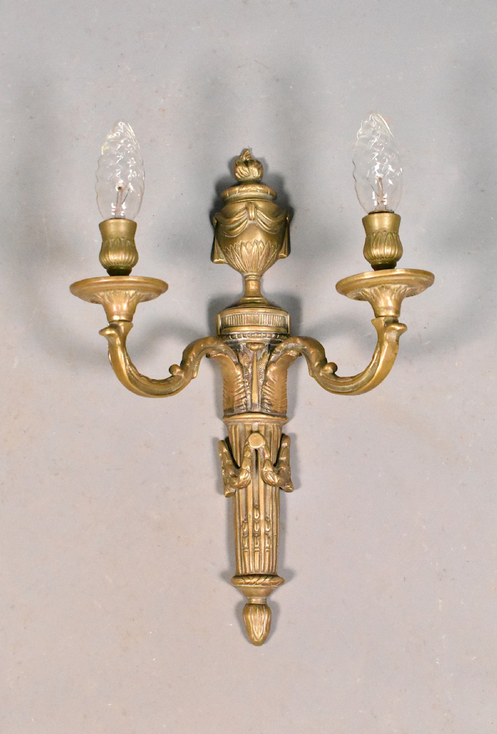 A French Napoleon III style cast bronze wall sconce featuring two curved candle arms, a central urn finial, and a fluted backplate.