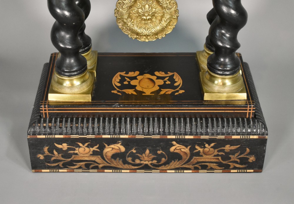 An ebonised Napoleon III portico mantel clock featuring floral marquetry inlays, twin barley twist columns, a white enamel dial with Roman numerals, and gilt brass mounts. View IX