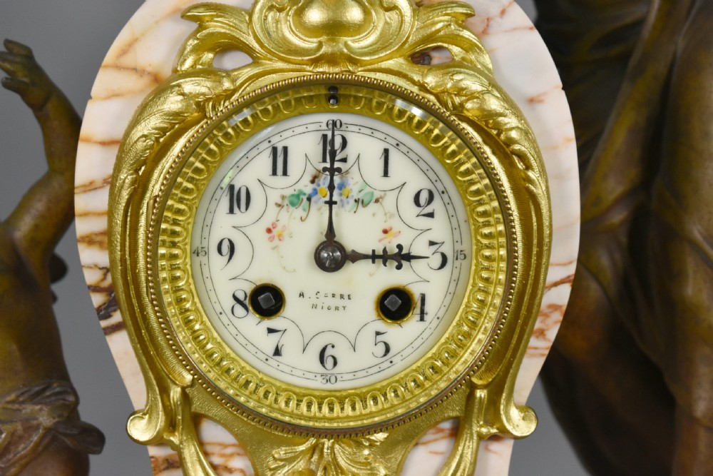 An Art Nouveau French mantel clock garniture featuring a central sculptural bronze figure beside an enamel clock face mounted on a pink veined marble base, flanked by two matching multi-arm candelabra. View VIII