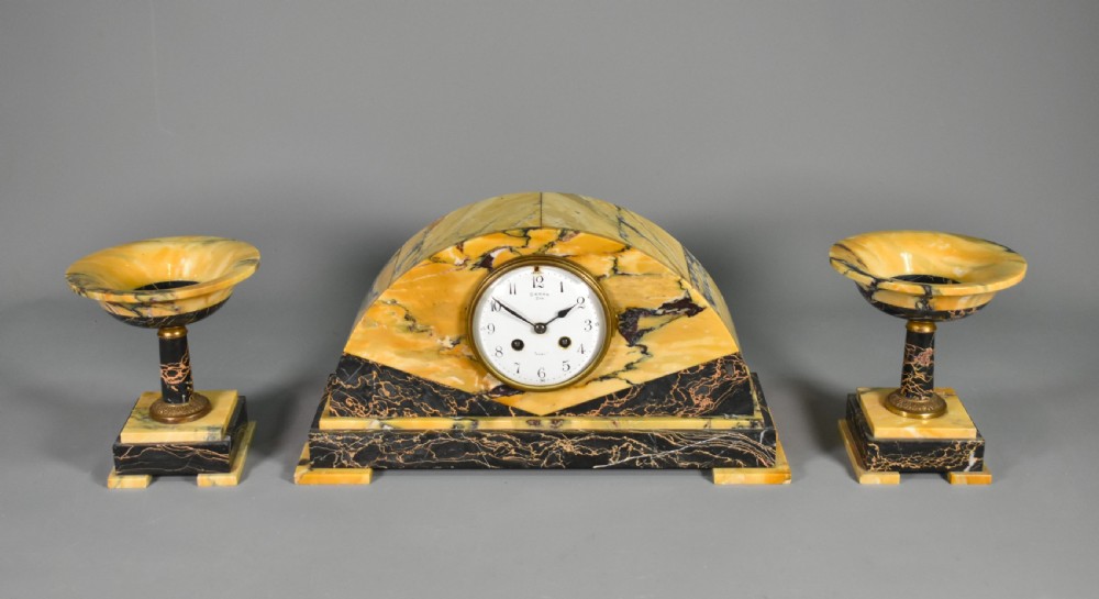 A French Art Deco mantel clock set featuring an arched yellow and black veined marble clock flanked by two matching marble chalice garnitures.