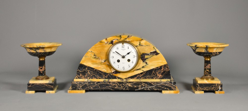 A French Art Deco mantel clock set featuring an arched yellow and black veined marble clock flanked by two matching marble chalice garnitures. View III