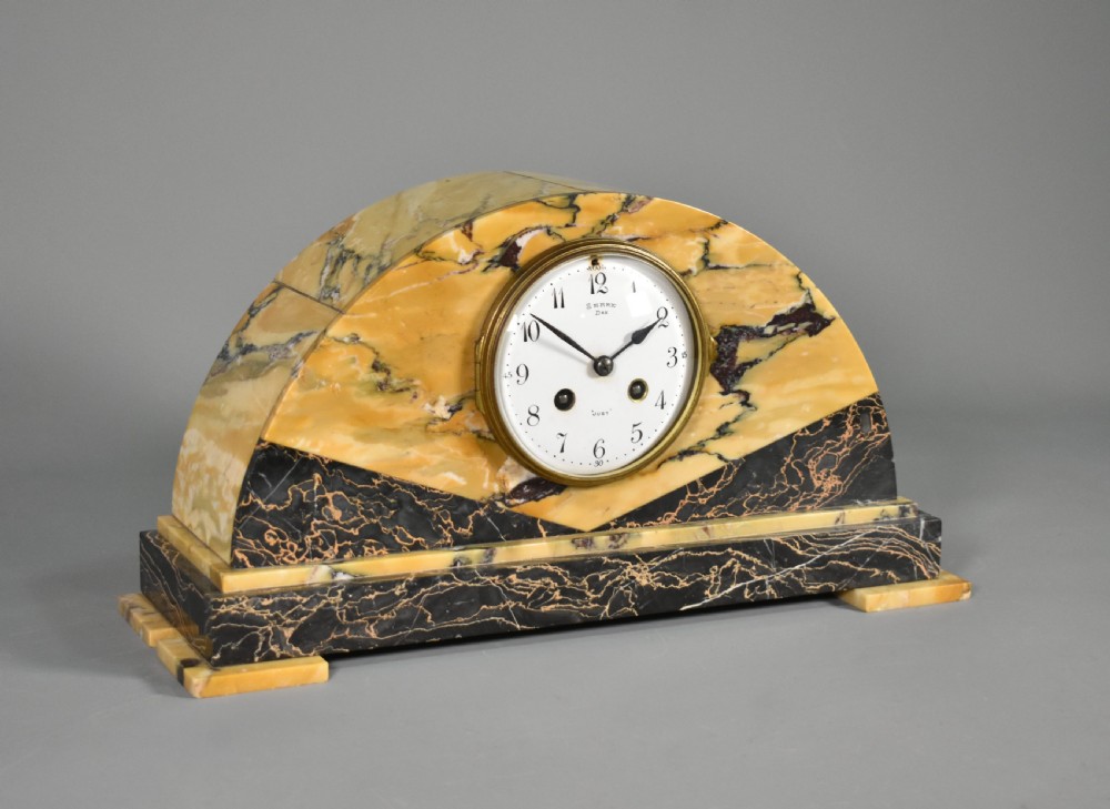 A French Art Deco mantel clock set featuring an arched yellow and black veined marble clock flanked by two matching marble chalice garnitures. View IV