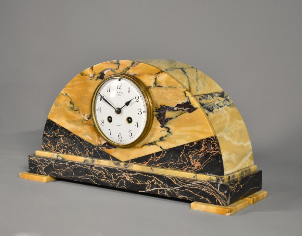 A French Art Deco mantel clock set featuring an arched yellow and black veined marble clock flanked by two matching marble chalice garnitures. View V