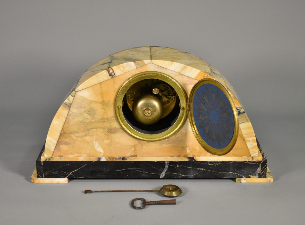 A French Art Deco mantel clock set featuring an arched yellow and black veined marble clock flanked by two matching marble chalice garnitures. View IX