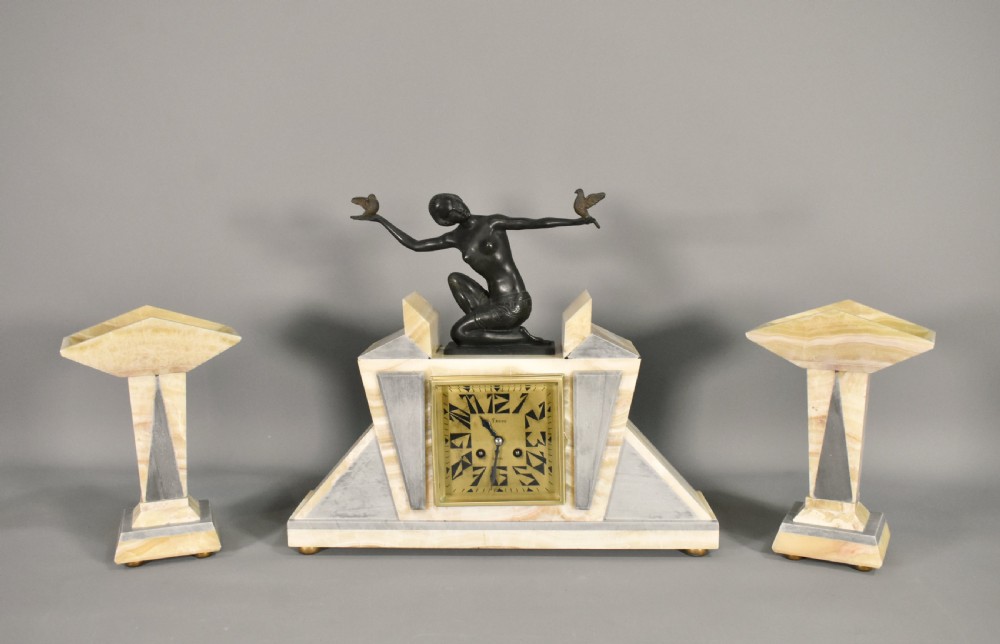 A three-piece French Art Deco clock garniture set featuring a central geometric onyx and marble clock topped with a bronze-finished figure of a female with birds, accompanied by two matching side pedestals. View II
