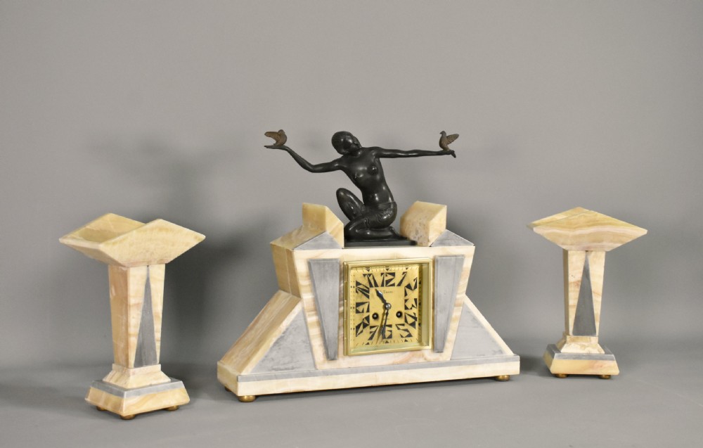 A three-piece French Art Deco clock garniture set featuring a central geometric onyx and marble clock topped with a bronze-finished figure of a female with birds, accompanied by two matching side pedestals. View III