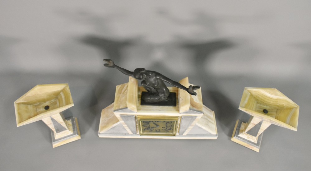 A three-piece French Art Deco clock garniture set featuring a central geometric onyx and marble clock topped with a bronze-finished figure of a female with birds, accompanied by two matching side pedestals. View XI