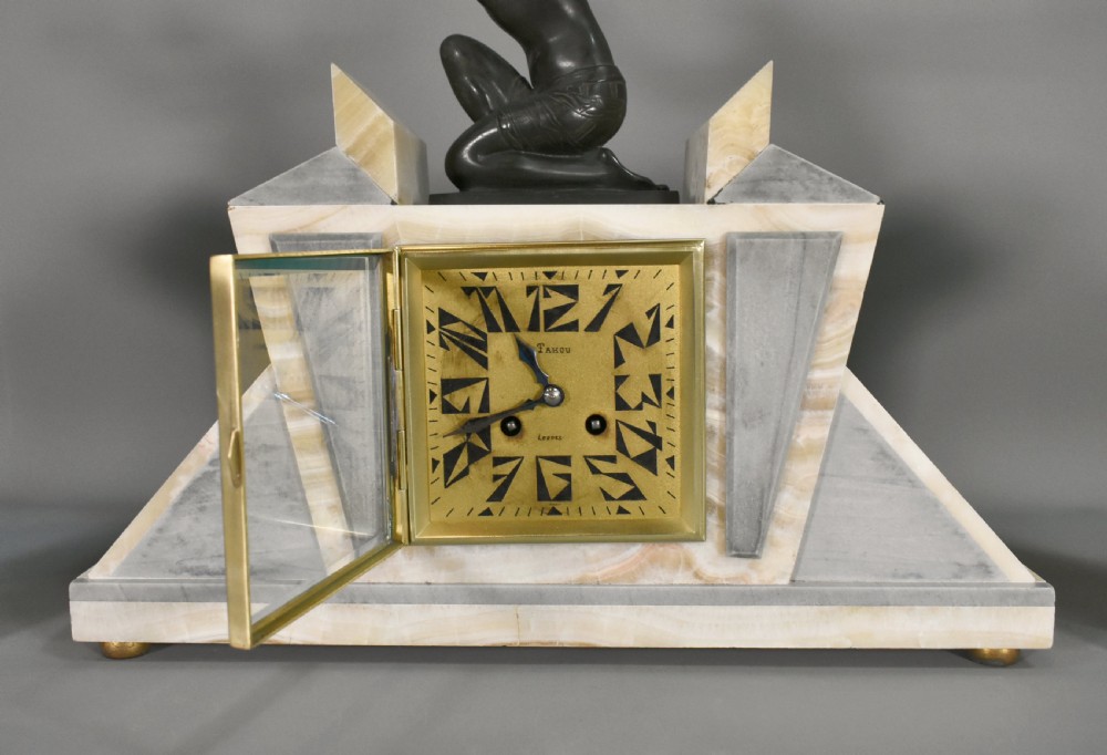 A three-piece French Art Deco clock garniture set featuring a central geometric onyx and marble clock topped with a bronze-finished figure of a female with birds, accompanied by two matching side pedestals. View XII