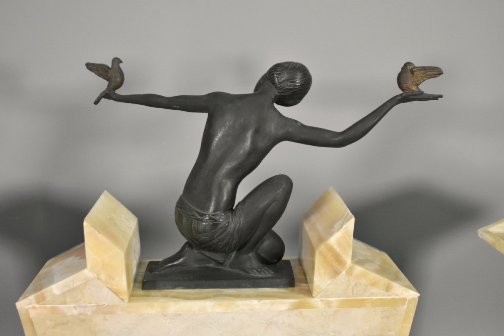 A three-piece French Art Deco clock garniture set featuring a central geometric onyx and marble clock topped with a bronze-finished figure of a female with birds, accompanied by two matching side pedestals. View XIV