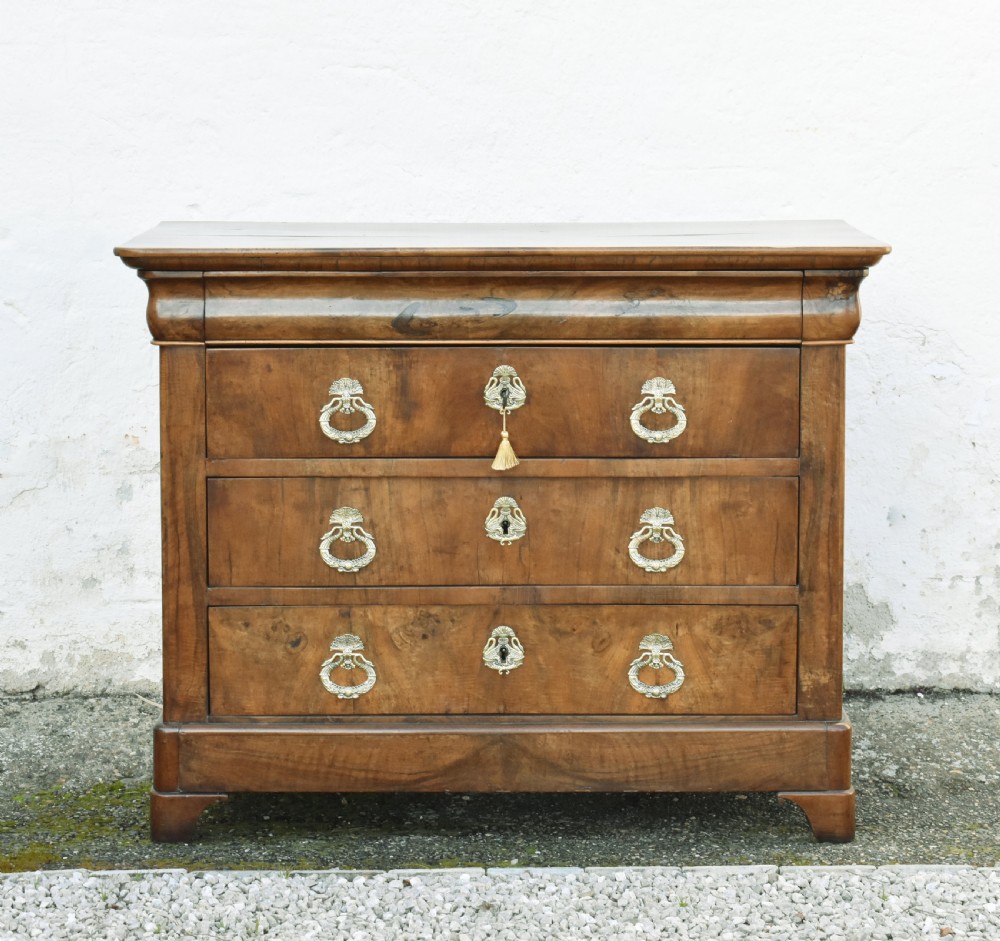A 19th-century French Louis Philippe walnut commode featuring a rounded top drawer, three lower drawers with brass drop handles, and a plinth base.