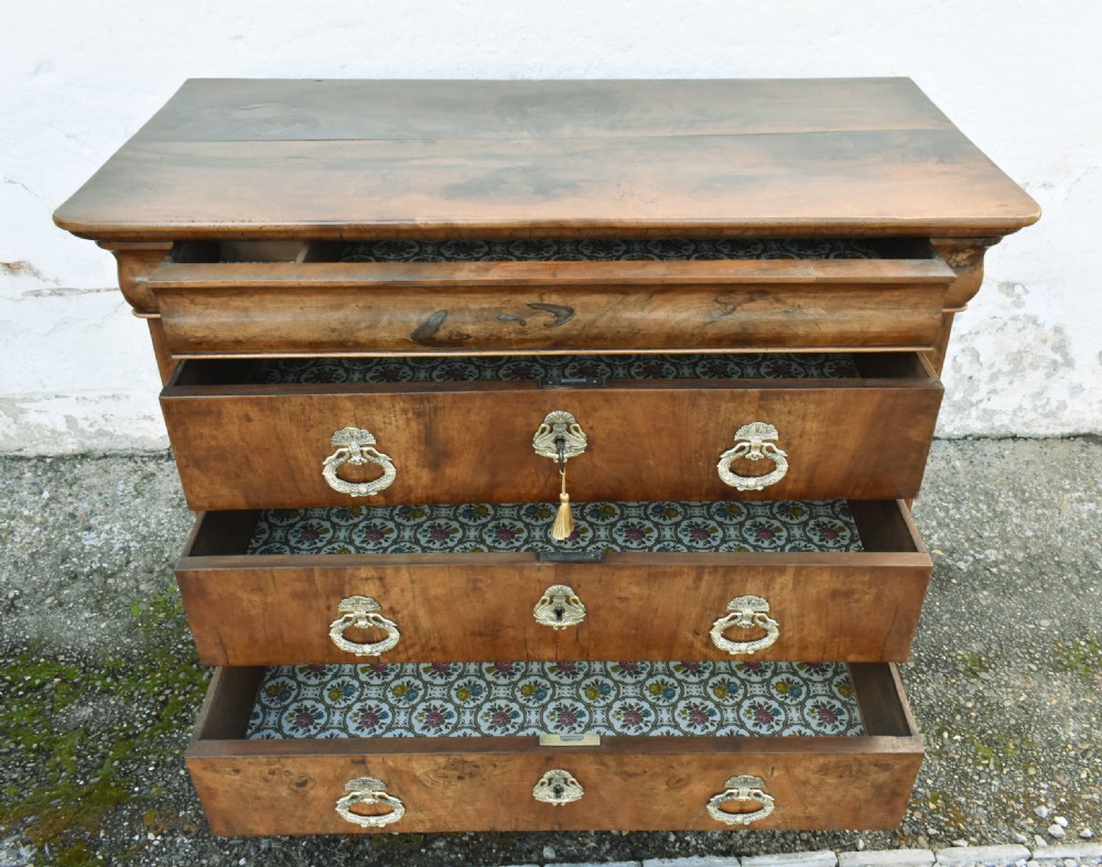 A 19th-century French Louis Philippe walnut commode featuring a rounded top drawer, three lower drawers with brass drop handles, and a plinth base. View XVI