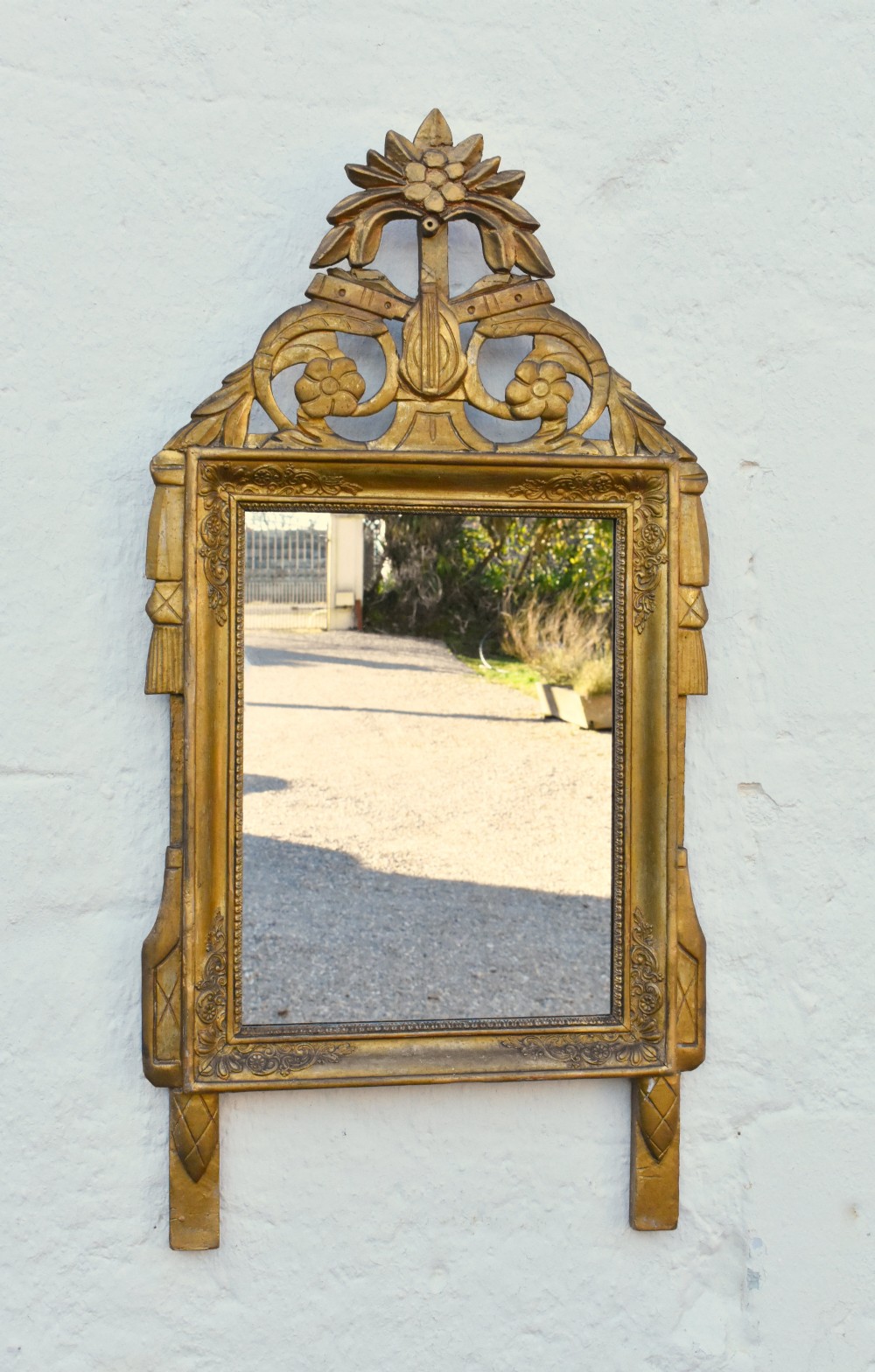 A rectangular French giltwood wall mirror featuring carved floral cresting and a gold leaf frame.