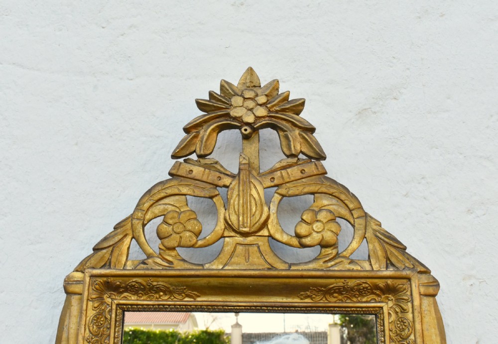A rectangular French giltwood wall mirror featuring carved floral cresting and a gold leaf frame. View X