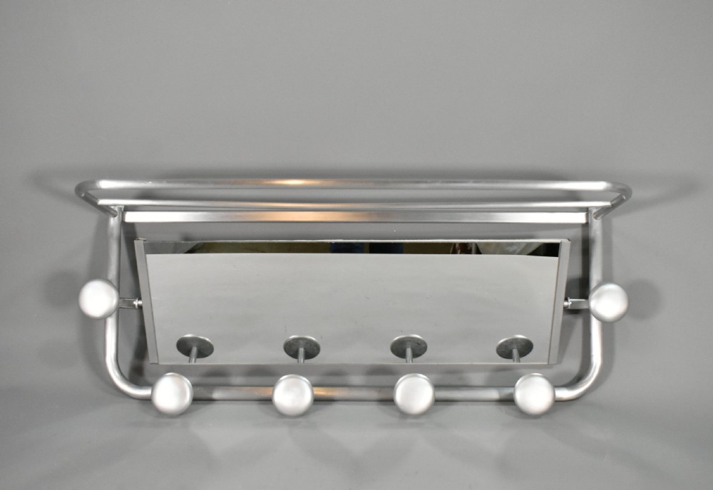 A French Art Deco wall-mounted tubular aluminium coat and hat rack featuring a central rectangular mirror, top slatted shelf, and spherical pegs.