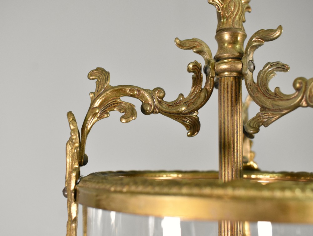 A cylindrical glass hall lantern featuring starburst engravings, gilt brass acanthus leaf mounts, and an interior multi-candle bulb holder. View X