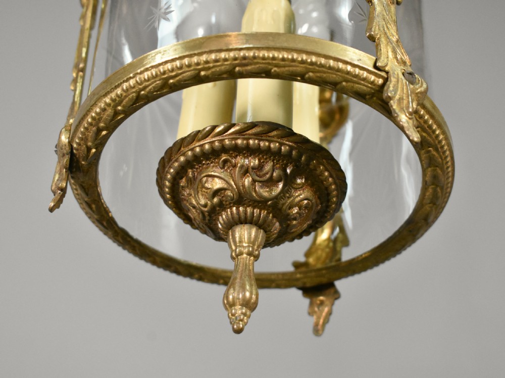 A cylindrical glass hall lantern featuring starburst engravings, gilt brass acanthus leaf mounts, and an interior multi-candle bulb holder. View XV