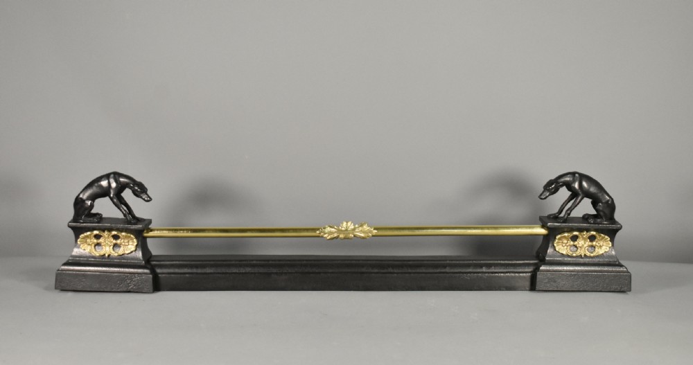 A 19th-century French fireplace fender featuring dark patinated metal greyhound sculptures resting on bases on either side of a polished brass rail with central gold-toned foliate detailing.