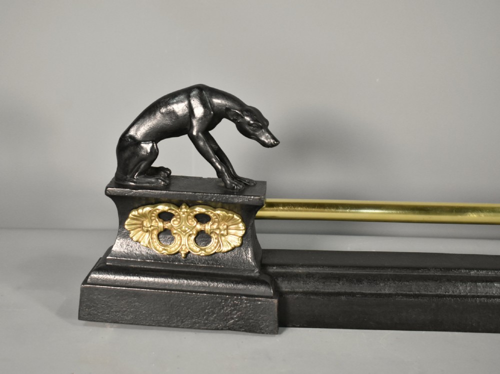 A 19th-century French fireplace fender featuring dark patinated metal greyhound sculptures resting on bases on either side of a polished brass rail with central gold-toned foliate detailing. View II