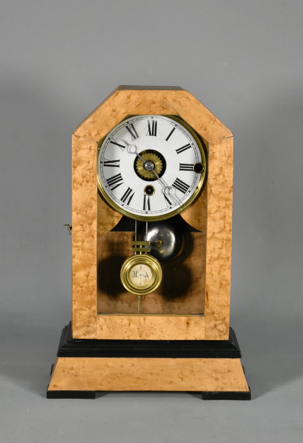 An antique mantel clock featuring a birdseye maple veneered arched case, ebonised plinth base, white enamel dial with Roman numerals, and a brass pendulum.