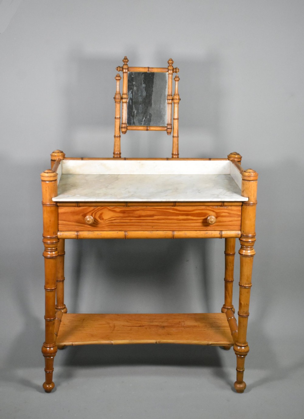 An antique French Napoleon III style washstand with a turned pine faux bamboo frame, marble top, lower shelf, and attached tilting mirror.