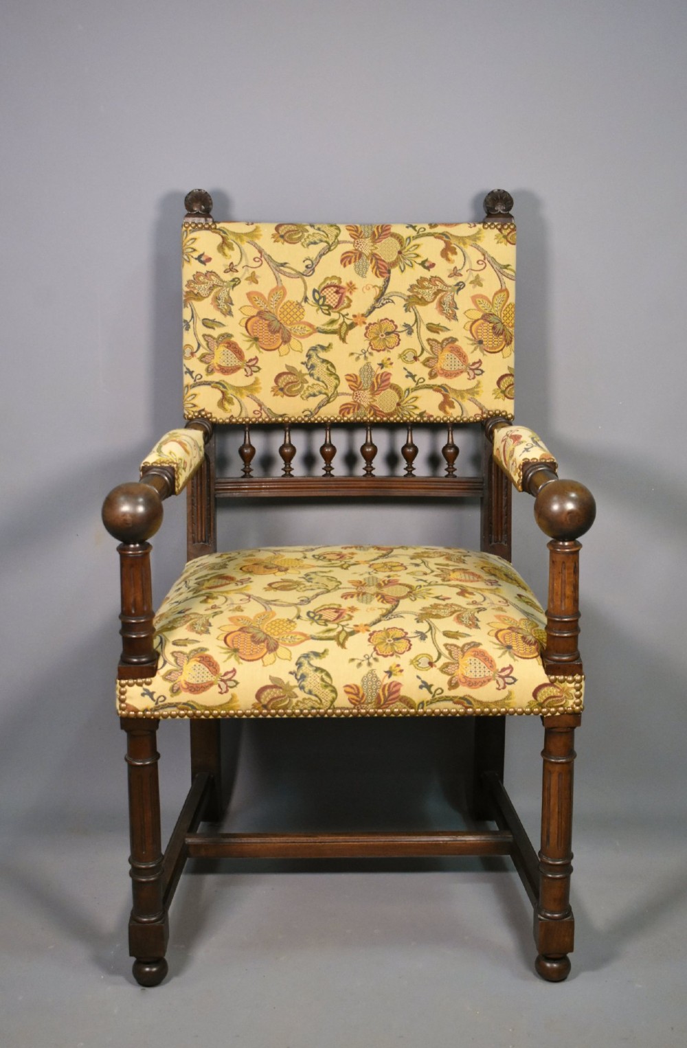 A French Renaissance Revival walnut armchair featuring yellow floral upholstery, brass stud trim, turned legs, spherical armrests, and a spindle gallery backrest.