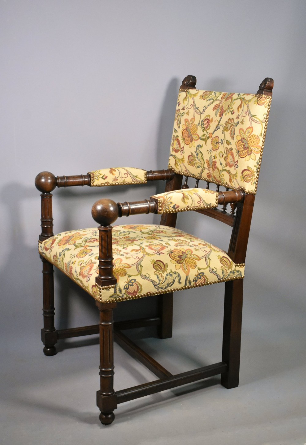 A French Renaissance Revival walnut armchair featuring yellow floral upholstery, brass stud trim, turned legs, spherical armrests, and a spindle gallery backrest. View V