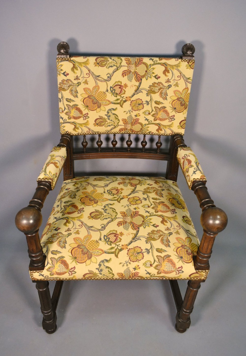 A French Renaissance Revival walnut armchair featuring yellow floral upholstery, brass stud trim, turned legs, spherical armrests, and a spindle gallery backrest. View VI