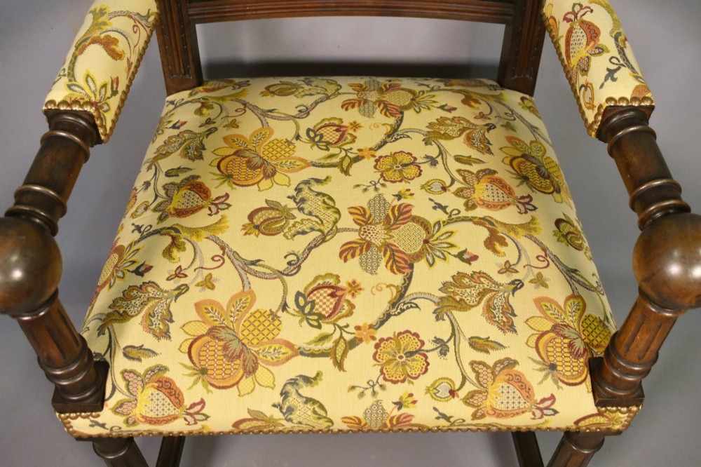 A French Renaissance Revival walnut armchair featuring yellow floral upholstery, brass stud trim, turned legs, spherical armrests, and a spindle gallery backrest. View X