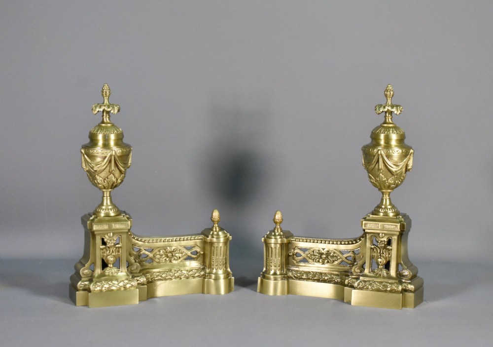 A pair of nineteenth-century French bronze fire dogs featuring carved urn finials, draped swags, and openwork bases.