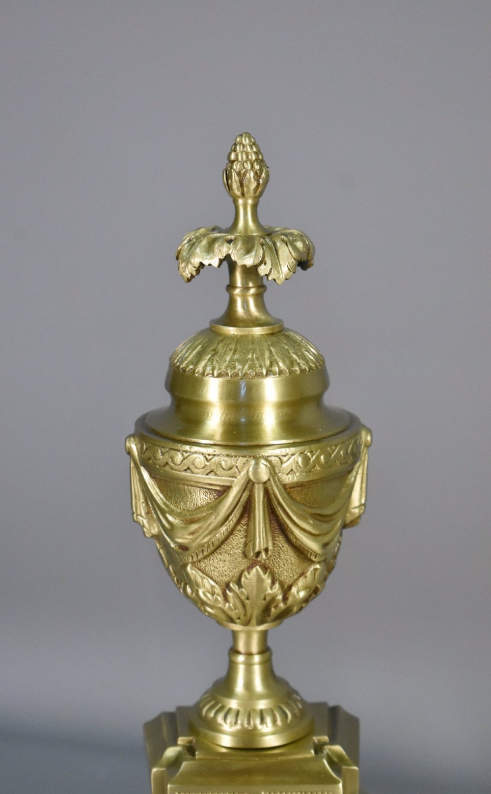 A pair of nineteenth-century French bronze fire dogs featuring carved urn finials, draped swags, and openwork bases. View II