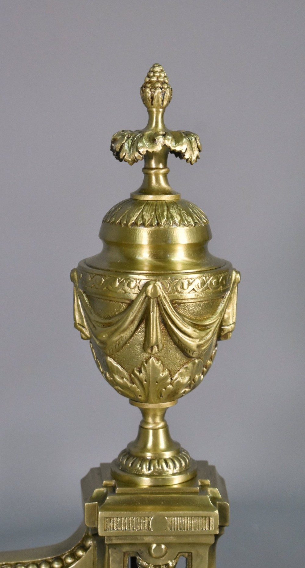 A pair of nineteenth-century French bronze fire dogs featuring carved urn finials, draped swags, and openwork bases. View IX