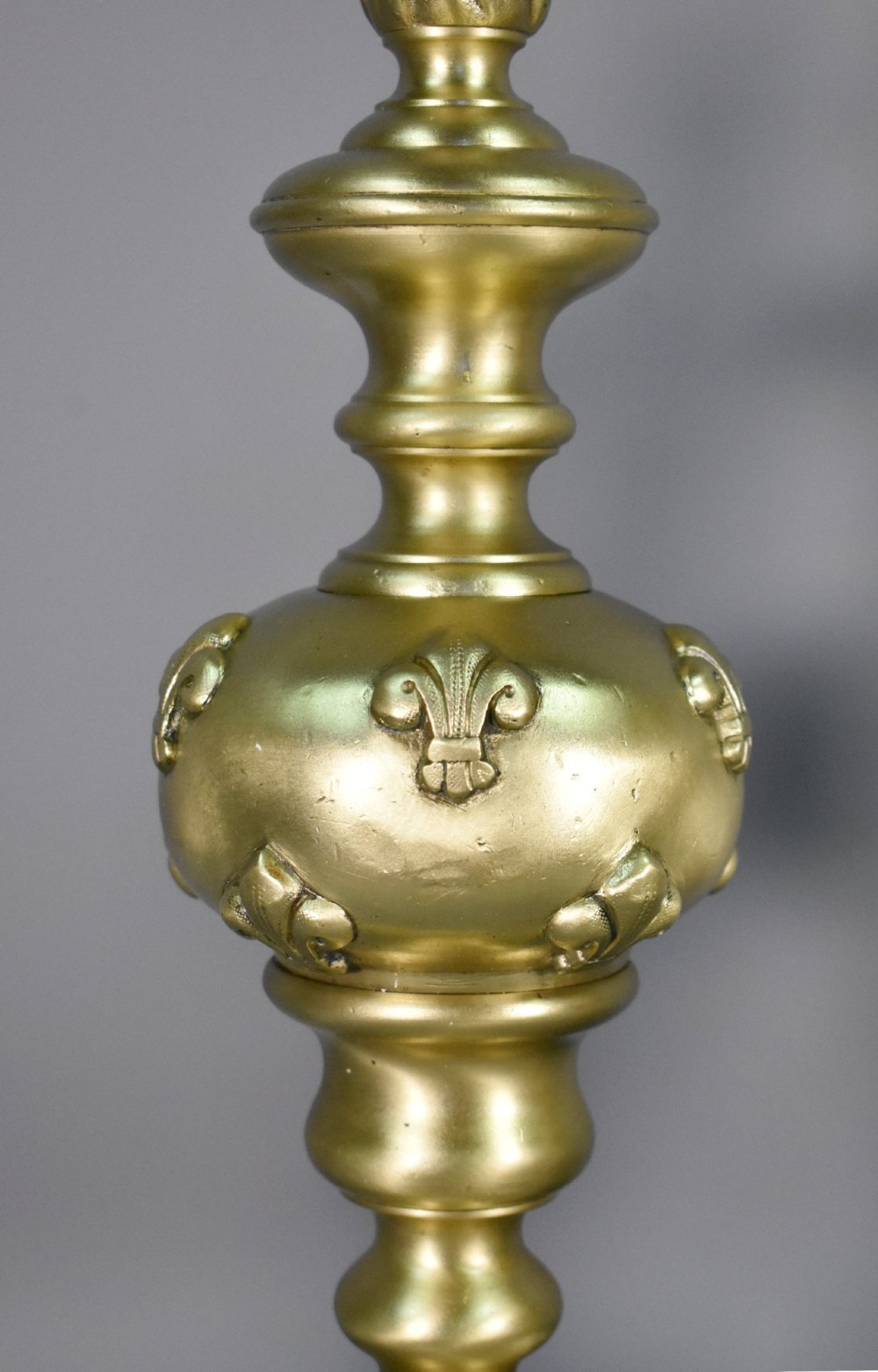 A pair of cast bronze Louis XIV style firedogs featuring baluster shafts, flame finials, and scrolled bases with relief mask carvings. View V