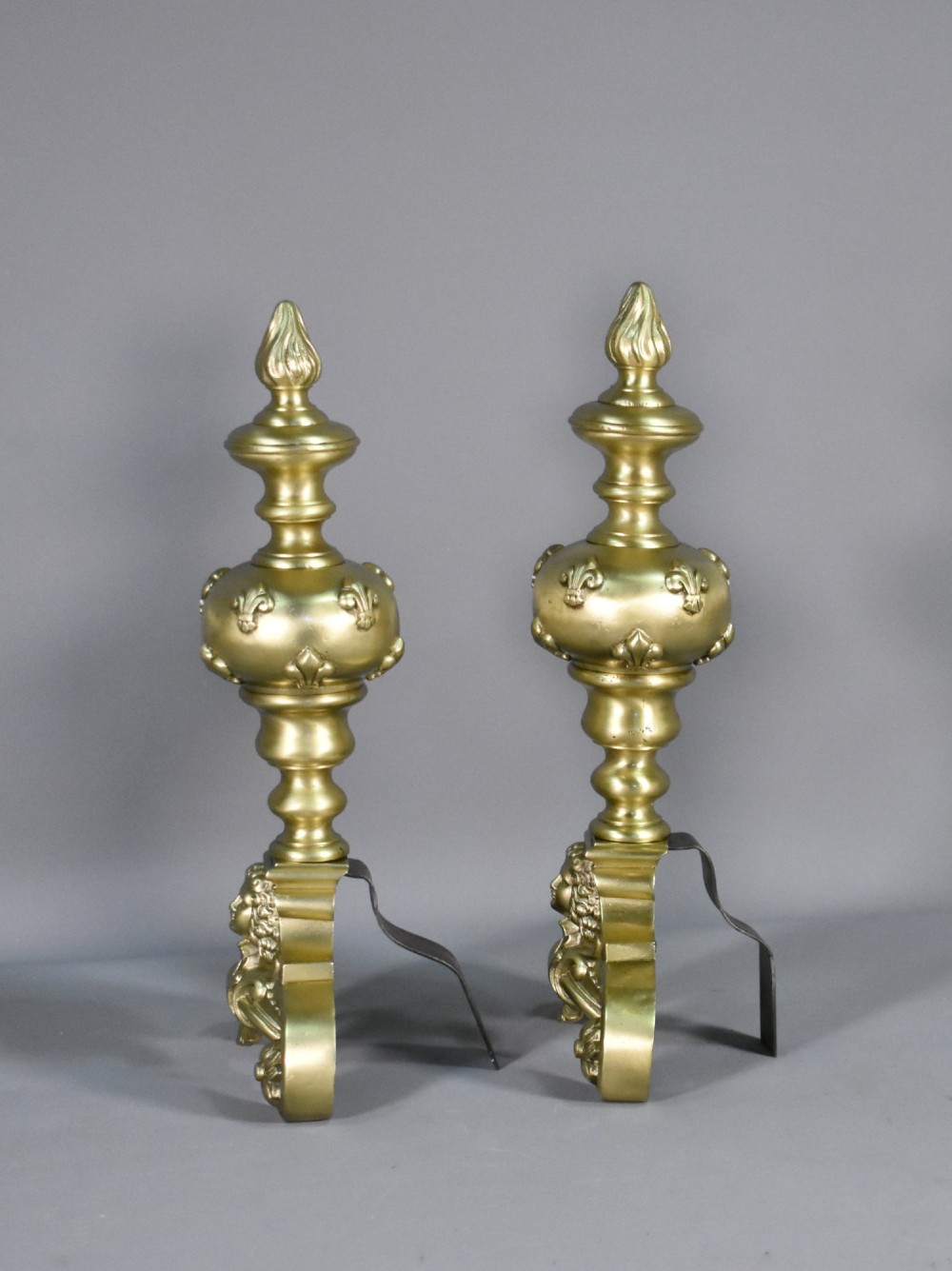 A pair of cast bronze Louis XIV style firedogs featuring baluster shafts, flame finials, and scrolled bases with relief mask carvings. View XI