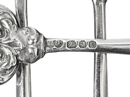fig 2. A set of eight sterling silver hors doeuvre skewers arranged in a fan shape, featuring ornate openwork scrollwork handles and tapered pins.