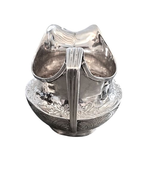 fig 1. A George III sterling silver cream jug with chased scroll decoration, an angular high loop handle, and a circular foot.