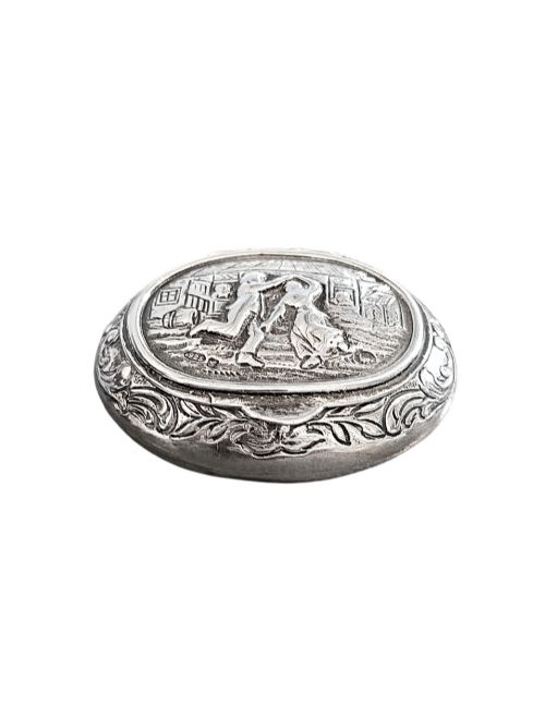 fig 1. An oval antique sterling silver snuff box featuring an embossed central scene of dancing figures, framed by scrollwork borders.