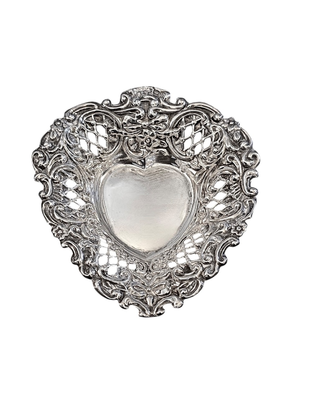 An Edwardian sterling silver heart-shaped bonbon dish featuring an ornate pierced lattice border with scrollwork and a smooth central reservoir.