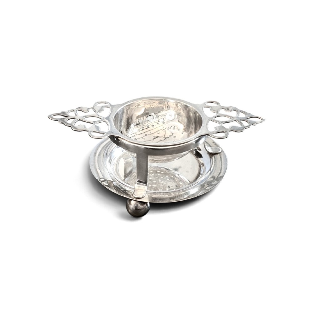 A sterling silver tea strainer featuring openwork pierced handles resting on a matching circular drip stand supported by spherical ball feet. View II