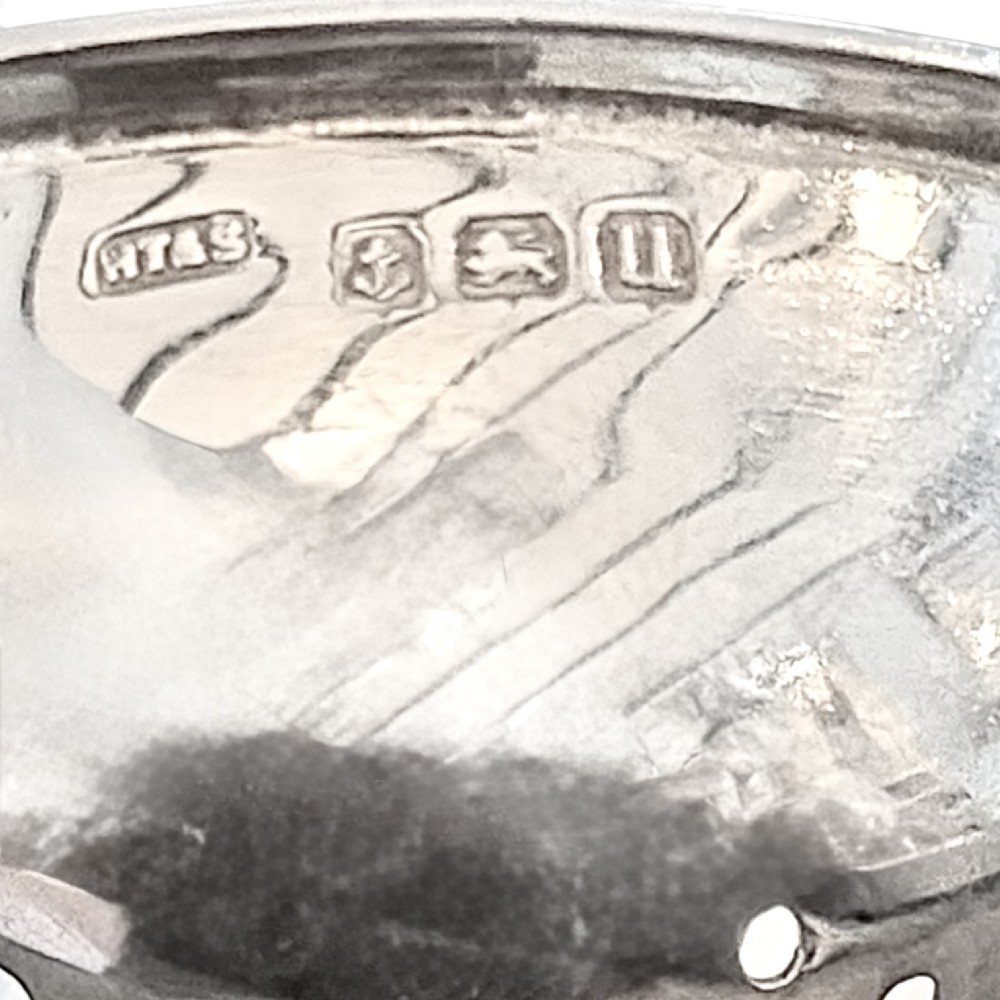 A sterling silver tea strainer featuring openwork pierced handles resting on a matching circular drip stand supported by spherical ball feet. View IV