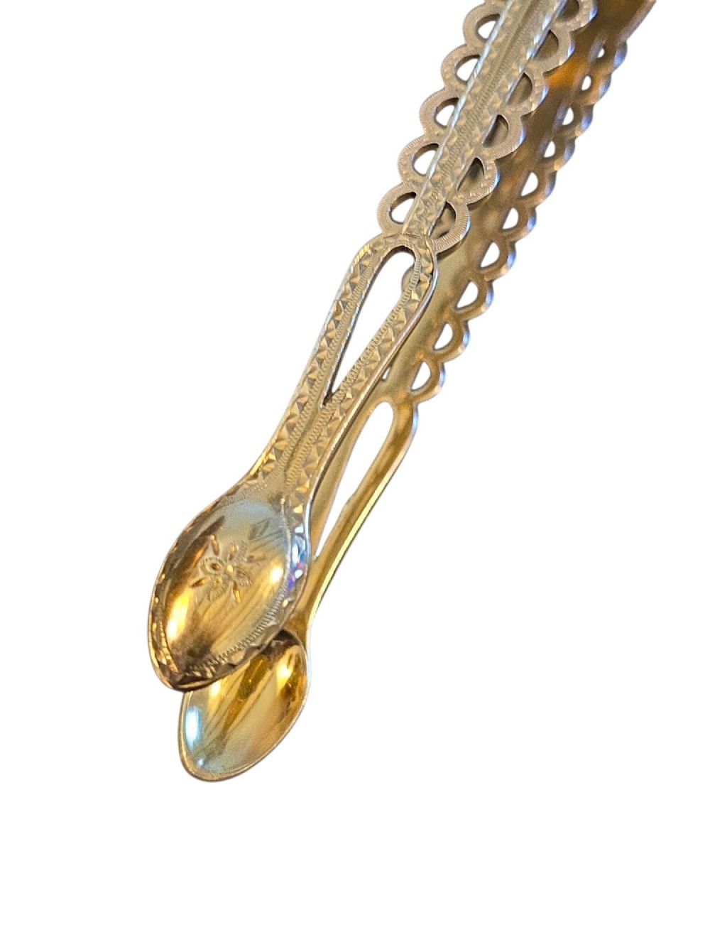 A pair of Victorian silver-gilt sugar tongs featuring decorative pierced arms and engraved spoon-shaped ends. View II