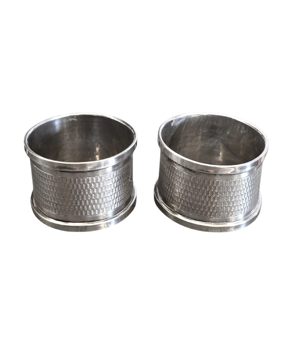 A pair of oval sterling silver napkin rings featuring an engine-turned textured band and plain polished edges. View II