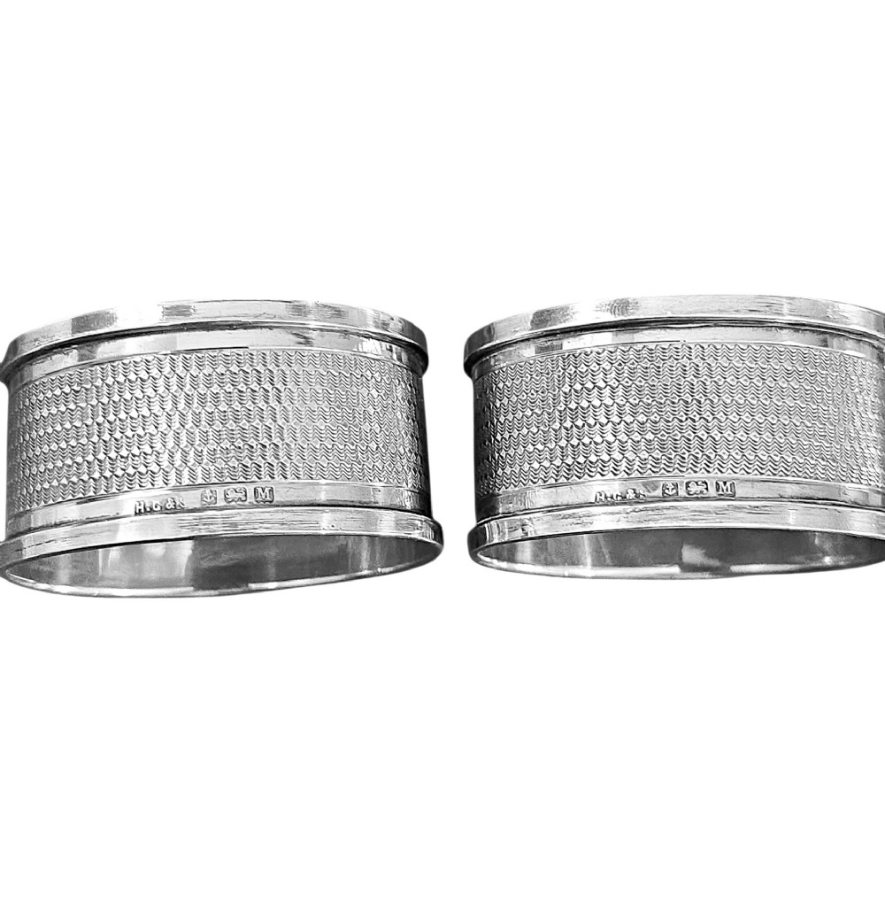 A pair of oval sterling silver napkin rings featuring an engine-turned textured band and plain polished edges. View IV