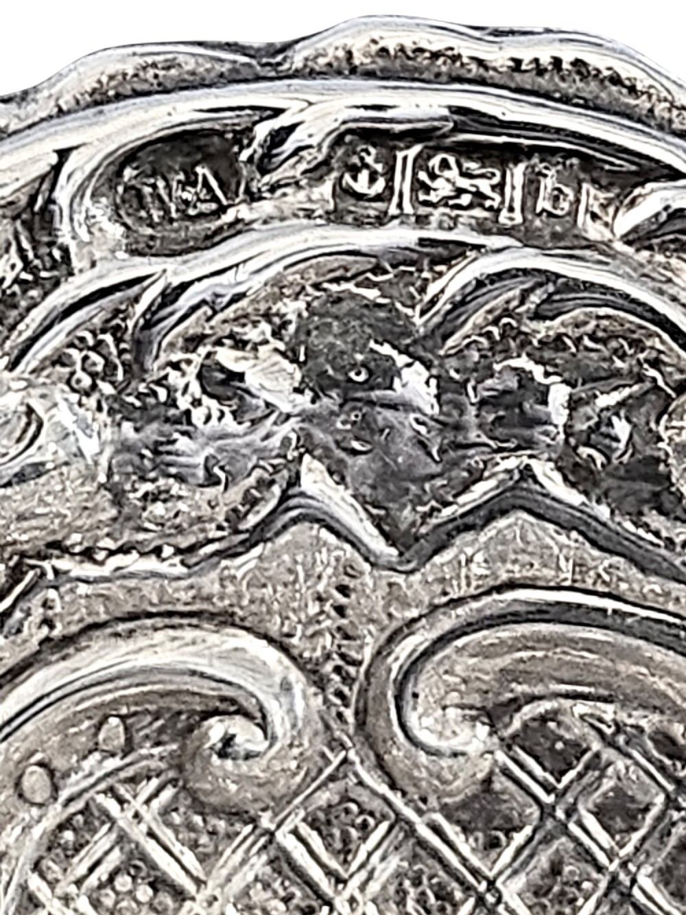 An antique oval sterling silver bonbon dish featuring embossed scrollwork, lattice detailing, a central cherub figure, and spherical ball feet. View V