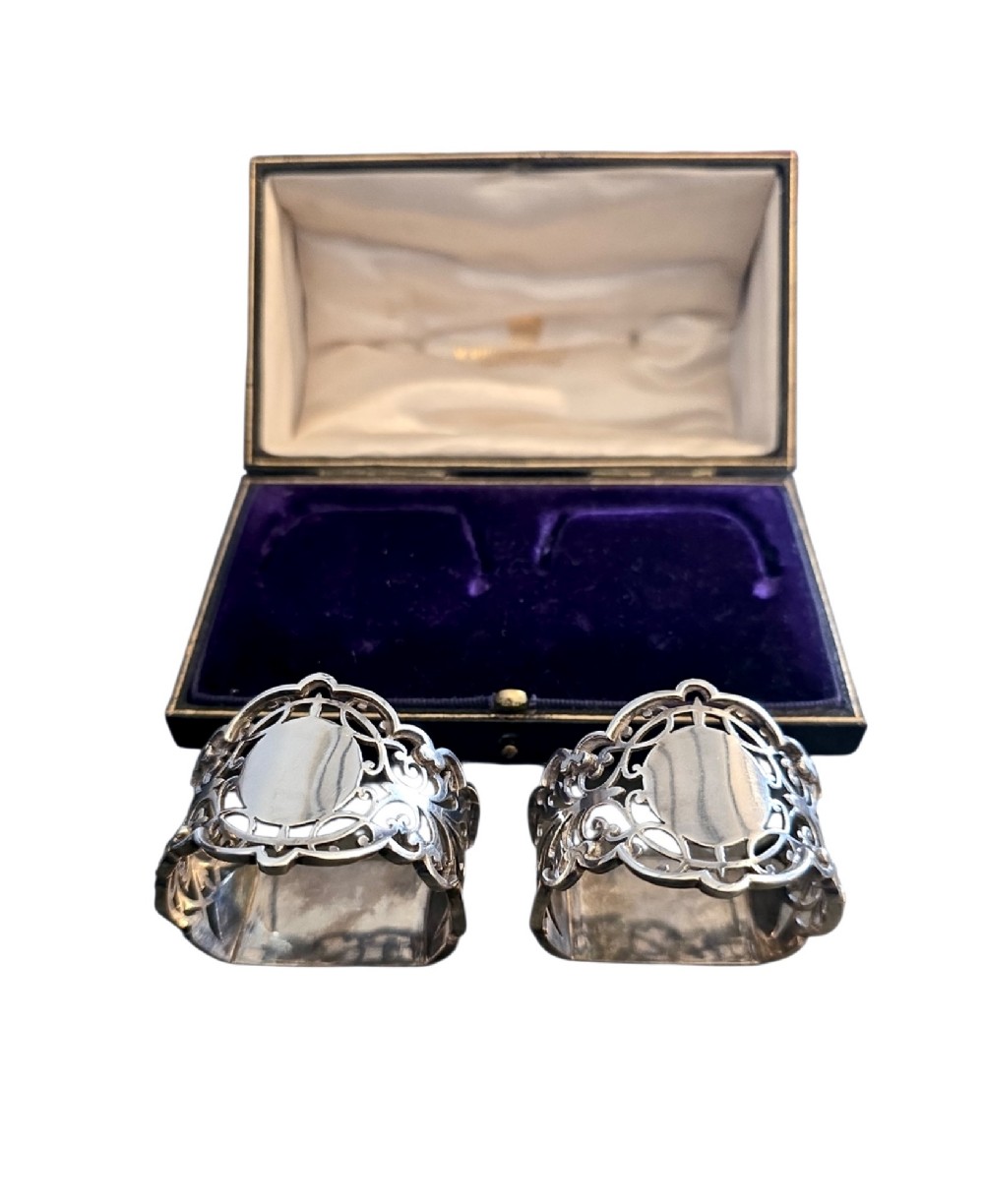 A pair of Edwardian pierced sterling silver napkin rings with unengraved cartouches presented in a dark velvet-lined fitted box. View II