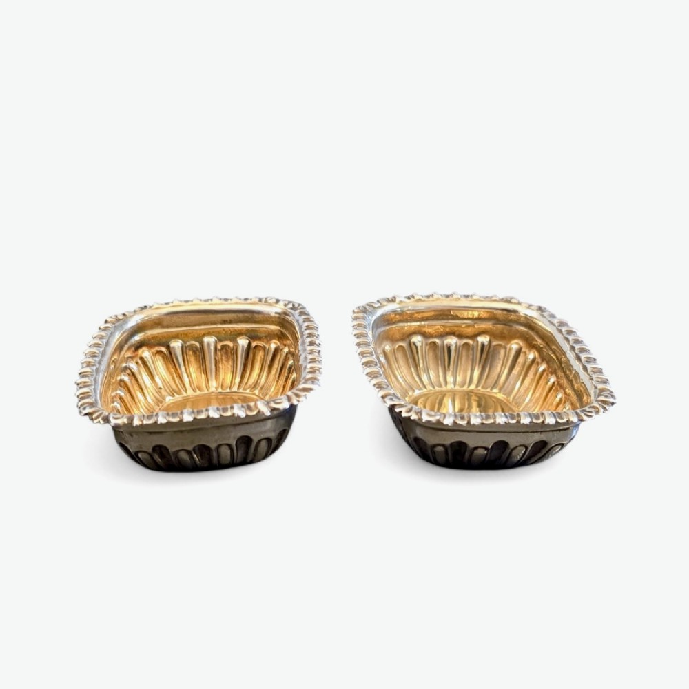 A pair of Edwardian sterling silver rectangular open salt cellars featuring fluted sides, gadrooned rims, and gilded interiors.