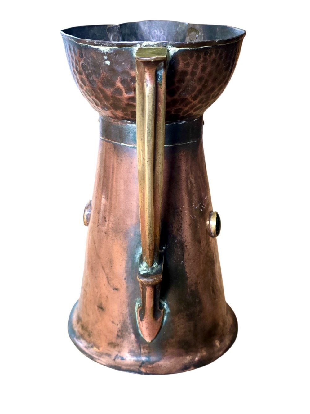 An antique Arts and Crafts copper jug featuring a planished finish, riveted collar, brass handle, and inset coloured cabochons. View II