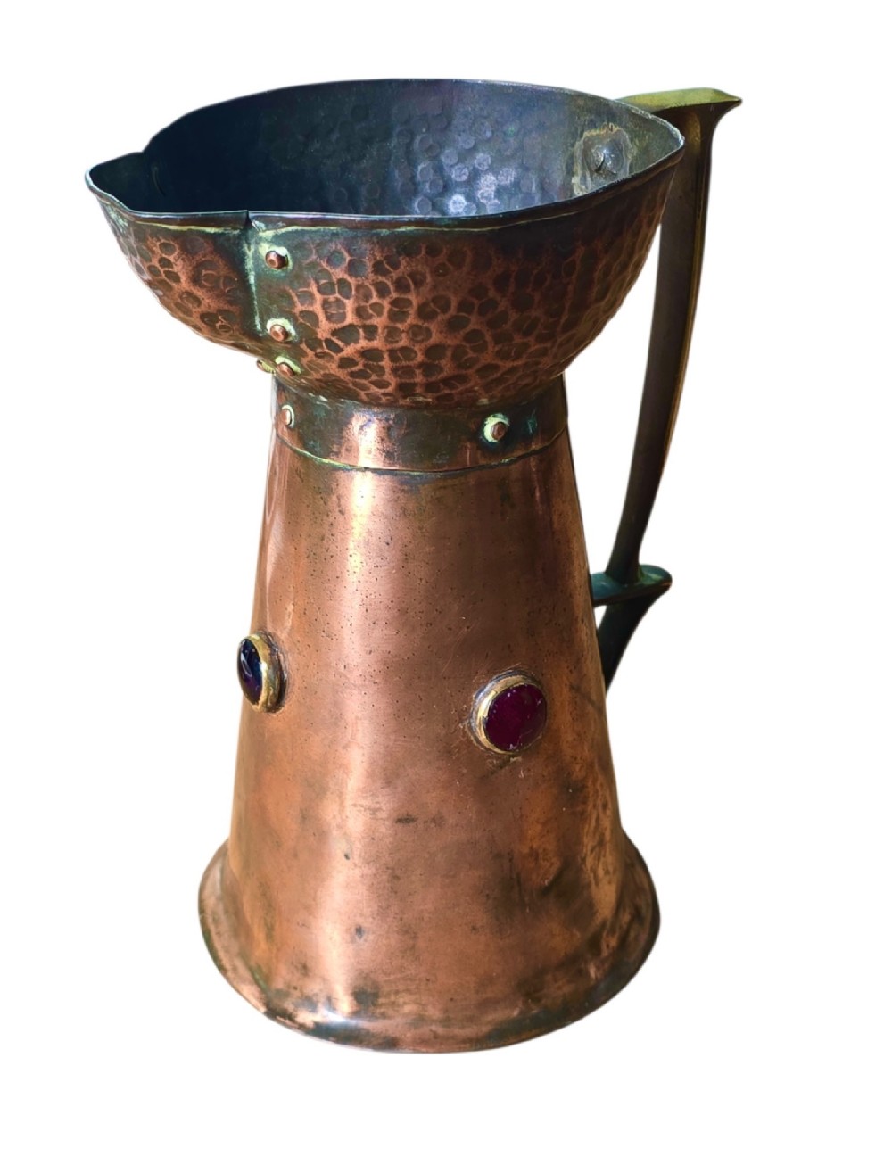 An antique Arts and Crafts copper jug featuring a planished finish, riveted collar, brass handle, and inset coloured cabochons. View V