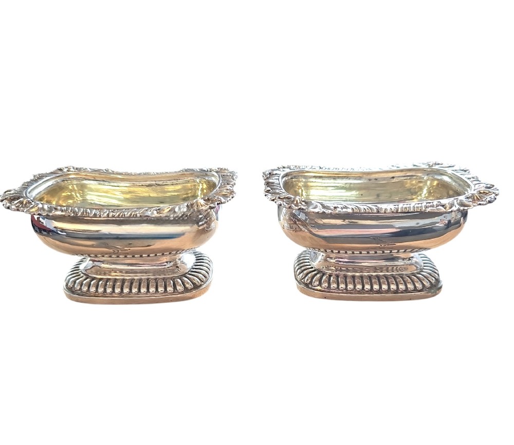 A pair of Regency sterling silver rectangular table salts featuring gadrooned rims and gilded interiors on shaped pedestal bases.