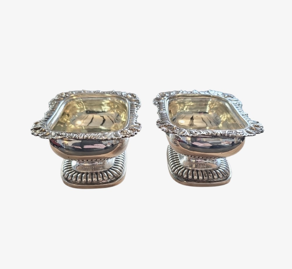 A pair of Regency sterling silver rectangular table salts featuring gadrooned rims and gilded interiors on shaped pedestal bases. View II