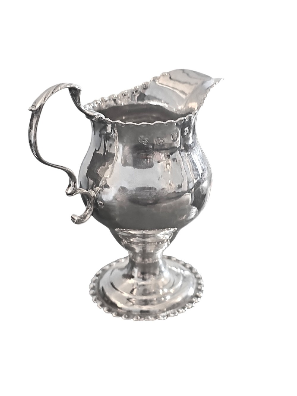 A George III sterling silver cream jug featuring a baluster shape, scalloped rim, double-scroll handle, and pedestal base.